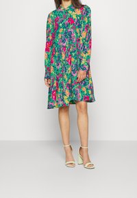 Blumenkleid mit langen Ärmeln und Kragen, das lebendige grüne, pinke, gelbe und orangefarbene Muster aufweist. A-Linie Silhouette mit einem fließenden Saum.
