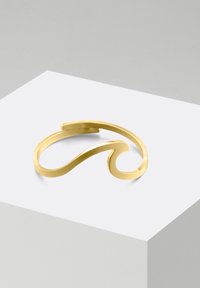 Goldfarbener Armreif mit elegantem, gewelltem Design, das durch sanfte Kurven und eine matten Oberfläche besticht. Minimalistisch ohne zusätzliche Verzierungen.