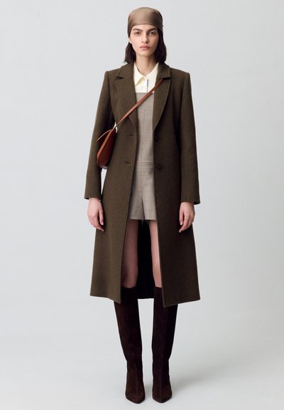 Cappotto in lana verde oliva con rever a scarpino, vestito a quadri beige sotto, stivali al ginocchio in suede marrone e una borsa coordinata.