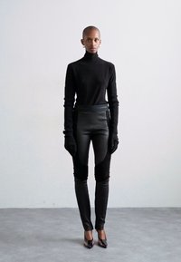 Pulover negru cu guler înalt și mâneci lungi, asociat cu pantaloni negri din piele ecologică cu panouri texturate și tocuri negre elegante.