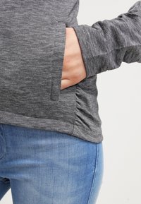 Main dans la poche d'une chemise à manches longues grise rayée portée avec un jean bleu clair.