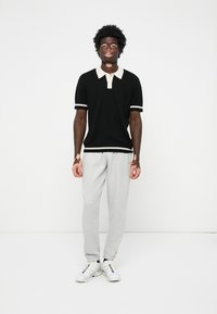 Fekete pólókrém színű gallérral és mandzsettákkal, szürke melegítőnadrág és fehér edzőcipő. Simító anyag, laza szabás, minimalista dizájn.