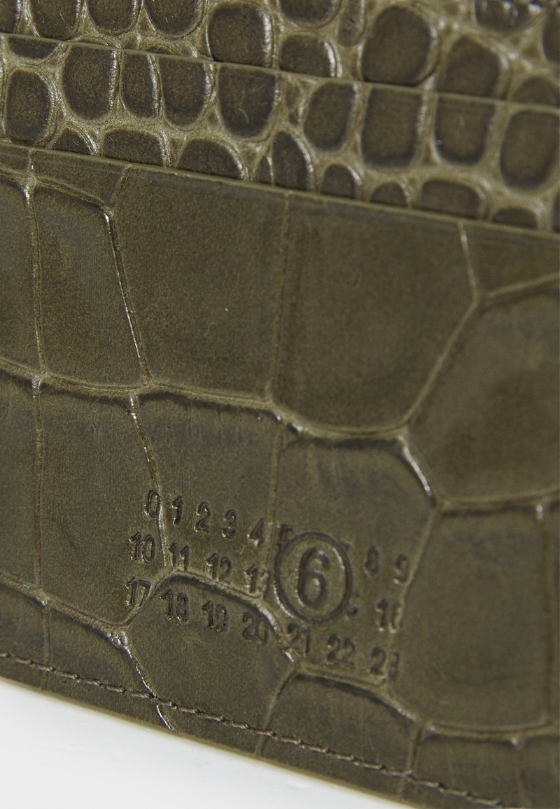 Olive green textured leather surface with reptile pattern and embossed numbers forming a date code including the number 6 circled.