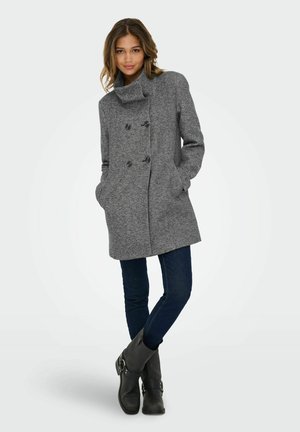 Manteau gris croisé avec un col haut et un tissu texturé. Comprend deux poches latérales, porté sur un jean foncé et des bottes noires.