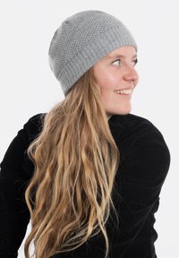 Szara dziana czapka beanie z teksturowanym wzorem i ściągaczem. Modelka ma długie, falowane włosy i nosi czarną bluzkę, pozując z boku.