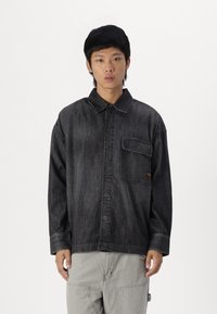 Camicia in denim scuro con colletto a punta, taschino sul petto e spalle scese. Presenta cuciture a contrasto e una vestibilità rilassata.