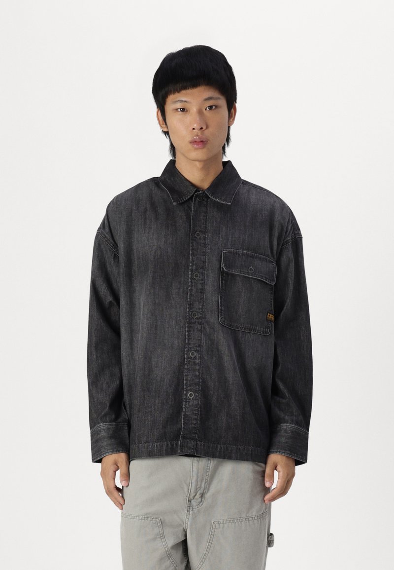 Camicia in denim scuro con colletto a punta, taschino sul petto e spalle scese. Presenta cuciture a contrasto e una vestibilità rilassata.