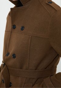 Bruine wollen jas met een dubbele knoopsluiting, zwarte knopen en een verstelbare taille. Bevat schouderepauletten en een gestructureerde kraag.