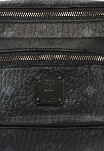 Zaino in pelle nera con superficie texture, hardware argentato e doppie cerniere. Presenta un'etichetta con il logo "MCM" e "München."