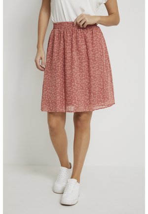 Vrouw draagt een roze, geplooide bloemenrok met een elastische tailleband, gecombineerd met witte sneakers en een wit topje.