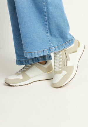 Lässige weiße und beige Sneaker mit seitlichem Reißverschluss und Schnürsenkeln, getragen zu hellblauen Jeans mit weitem Bein, vor hellem Hintergrund.