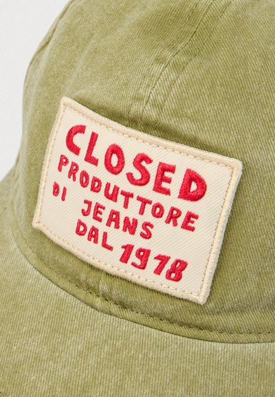 Καπέλο σε ελαιί πράσινο χρώμα από κορντόρι με ορθογώνιο μπεζ ένθετο. Το ένθετο φέρει κόκκινα κεντημένα γράμματα: "CLOSED PRODUTTORE DI JEANS DAL 1978".