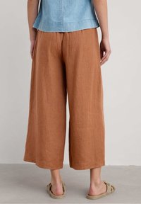 Brown linen wide-leg trousers with a textured finish, featuring a high waist and cropped length, worn with slip-on espadrille sandals.