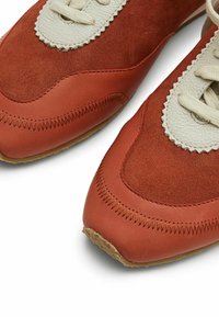 Raudoni nubuko ir odiniai sportiniai batai su smėlio spalvos akcentais ir tekstūruotu siuvimu. Suapvalintas pirštas ir raištelinė konstrukcija. Guma padas.