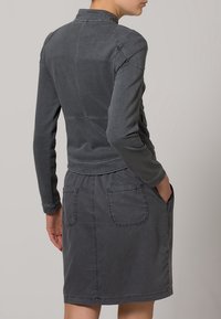 Vestido gris de mezcla de algodón con mangas largas, cuello con solapa, detalles cosidos y bolsillos delanteros. Textura suave y diseño informal.