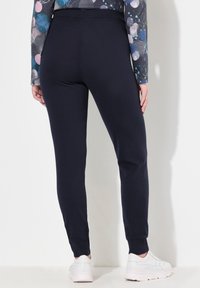 Granatowe dresy o dopasowanym kroju, z prążkowanym pasem i mankietami. W zestawie z białymi trampkami, prezentujące swobodny styl.