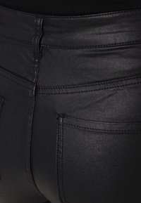 Černé úzké džíny z materiálu podobného kůži s hladkým povrchem, obsahující zadní kapsy a jemné švy bez viditelného kovového příslušenství.