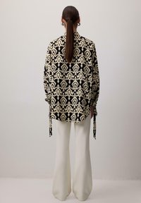 Cămașă supradimensionată cu model alb-negru, având legători la mâneci, combinată cu pantaloni evazați albi. Material fin și croi lejer.