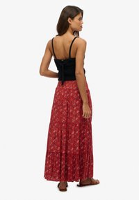 Top negro de punto con tirantes ajustables, combinado con una falda larga roja con estampado floral, con volantes y diseño fluido. Sandalias marrones en los pies.