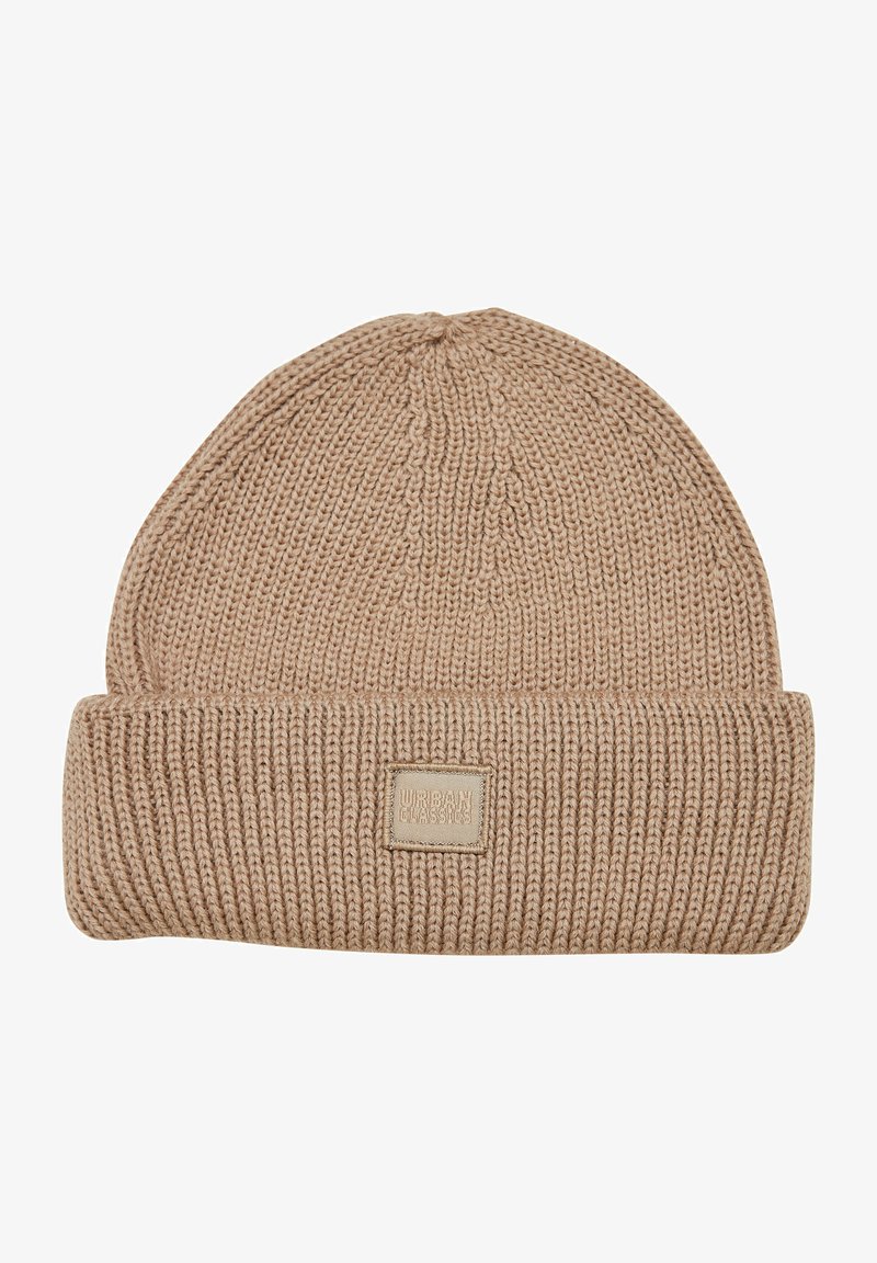 Beige knitted beanie hat with a folded cuff and a square label. Textured, soft material with a ribbed pattern.