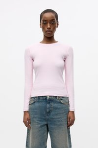 Camicetta a maniche lunghe di un delicato rosa chiaro con scollatura rotonda, realizzata in un tessuto morbido e liscio, abbinata a jeans in denim blu dal taglio morbido.