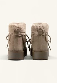 Botine din suede taupe până la glezne, cu interior din blană sintetică, guler căptușit și șireturi decorative. Talpă robustă din cauciuc cu un tăvăluch pentru aderență.