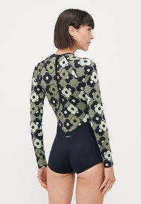 Langermet badedrakt med blomstermønster i grønt og svart, åpen ryggdesign, med ensfarget navy bunn og Roxy-logo.