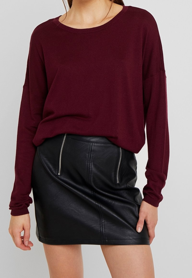 Top a maniche lunghe in maglia bordeaux abbinato a una mini gonna nera in similpelle con dettagli in zip argentati sulle tasche.