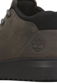Scarpa in pelle marrone con dettagli neri, lacci grigi, superficie testurizzata e logo di marca. Presenta una suola in gomma resistente e dettagli cuciti.