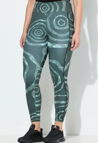 Leggings de cintura alta en color verde azulado oscuro con patrones circulares y ondulados en azul claro. Elaborados con un material elástico y con un detalle de cremallera lateral.