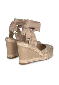 Beżowe sandały na koturnie z plecionym paskiem wokół kostki, z haftowanym wzorem z przodu i jutowym wykończeniem na obcasie.