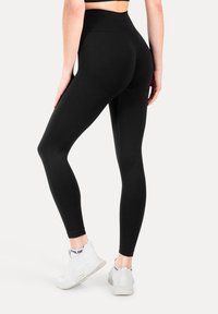Leggings negras de cintura alta, hechas de una tela elástica, con una textura suave y un diseño ajustado, combinadas con zapatillas blancas.