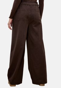 Bruine wijde broek met een elastische tailleband, voorzien van twee achterzakken en een zachte katoenen textuur. Eenvoudig ontwerp en losse pasvorm.