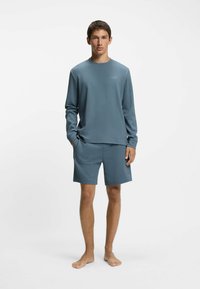 Vaaleansininen pitkähihainen paita ja siihen sopivat shortsit teksturoidusta kankaasta. Paidassa on pyöreä kaula-aukko ja hillitty logotikkaus.