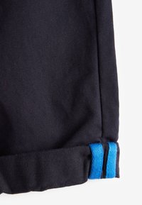 Primer plano de tela negra con un dobladillo doblado que presenta dos rayas azules paralelas en el borde.