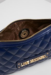 Námořnická prošívaná kabelka z umělé kůže s pozlacenými detaily, se zvýrazněným logem "LOVE MOSCHINO" a vzorovanou hnědou podšívkou.