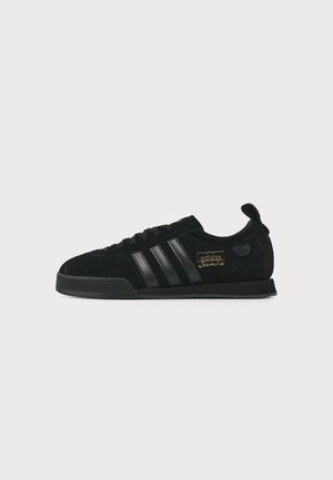 Μαύρο αθλητικό παπούτσι Adidas Samba με επάνω μέρος από σουέτ, τρεις δερμάτινες ρίγες, υφή στη σόλα και χρυσό λογότυπο στο πλάι, εμφανιζόμενο σε πλάγια όψη.