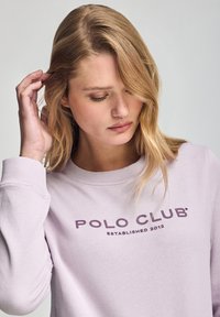 Sudadera lavanda con cuello redondo, puños acanalados y "POLO CLUB ESTABLISHED 2012" impreso en púrpura oscuro en el pecho. Textura suave.