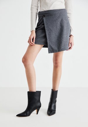 Herringbone-patterned gray skirt with a wrap design, featuring a button closure. Paired with black leather ankle boots with pointed heels.