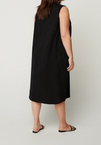 Černé bezramínkové šaty s volným střihem, délka až ke kolenům, texturovaný povrch a boční rozparky. Kombinováno s plochými černými sandály se vzorovanými popruhy.