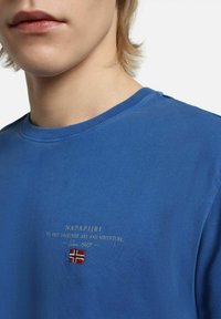 T-shirt in cotone blu a girocollo con logo e testo ricamati in oro, e un piccolo dettaglio con la bandiera norvegese sotto il testo.