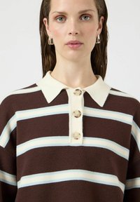 Polówka w brązowo-kremowe paski z plisą zapinaną na guziki. Miękka w dotyku, z jasnoniebieskimi paskami i klasycznym kołnierzykiem.