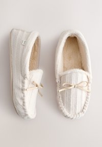 Paire de chaussons mocassins tricotés couleur crème avec une doublure douce en peluche et des nœuds en ruban beige sur un fond clair.