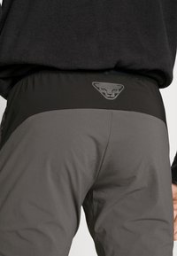 Gray hiking pants with a black waistband featuring a logo. The material appears textured, with panels of varying shades of gray.