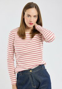 Camicia a maniche lunghe a righe in crema con righe rosa. Materiale in cotone, vestibilità morbida. Indossata con jeans in denim blu con un dettaglio di bottone.