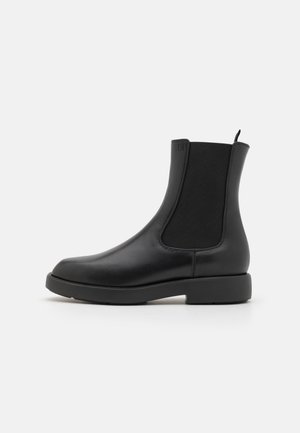 Black leather ankle boots with elastic side panels, rounded toe, and low textured rubber sole. Minimalist design with back pull tab.