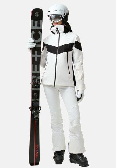 Skidragt med en hvid og sort jakke, hvide bukser og sorte skistøvler, holder sorte ski med røde og grå accenter.