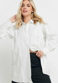 Camicia bianca a maniche lunghe con bottoni, dal taglio morbido, caratterizzata da ricami testurizzati sulle maniche e delicate cuciture verticali sul davanti.