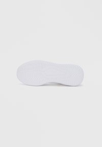 Beli podplat superge z teksturiranim vzorcem, ki vsebuje utore za oprijem. Dizajn vključuje neopazen logotip blizu pete.