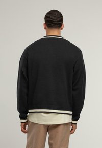 Černý pletený svetr s žebrovaným bílým límcem a manžetami, s uvolněným střihem a texturovanou tkaninou. Přes lehkou košili.